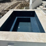 Spa attached to pool, with a dark blue integrate tile, with an outline with a beige tile. The spa features 2 levels one for seating, and a lower level for leg extension.