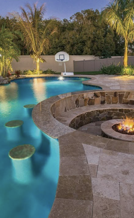 Curved modern pool with submerged bar stools and built-in fire pit lounge, surrounded by tropical landscaping