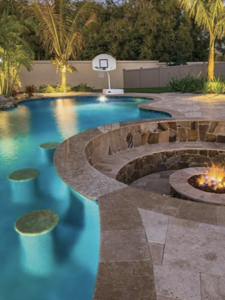 Luxury Spillover Pool & Spa with Water Features | Custom Backyard Design Curved modern pool with submerged bar stools and built-in fire pit lounge, surrounded by tropical landscaping